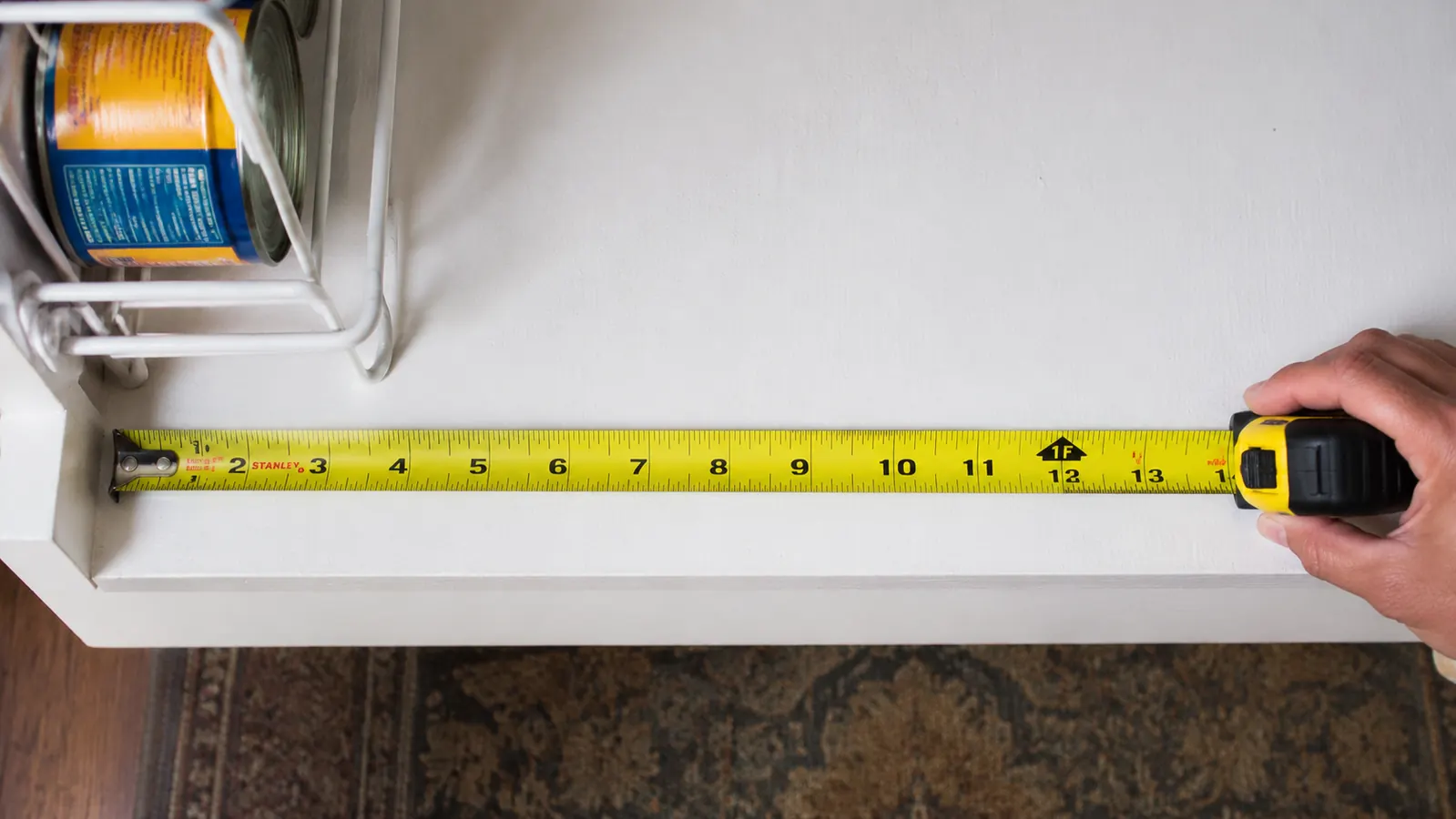 Tape measure laid flat on a pantry shelf showing 14-inch shelf depth measurement next to a can dispenser rack